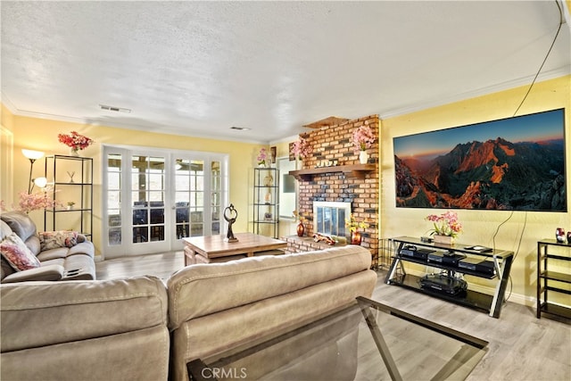 living room featuring french doors, ornamental molding, a brick fireplace, light wood-type flooring, and a textured ceiling