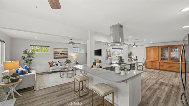 kitchen featuring a center island with sink, a kitchen breakfast bar, sink, island range hood, and wood-type flooring