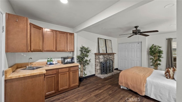 bedroom with ceiling fan, sink, a stone fireplace, dark hardwood / wood-style floors, and a closet