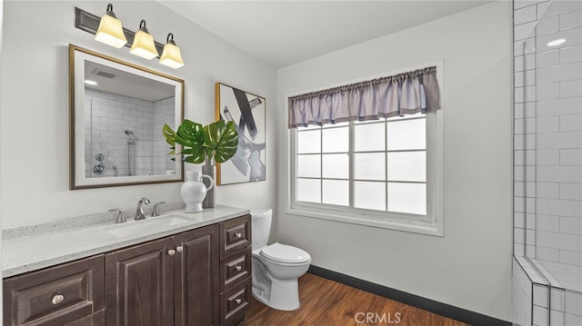 bathroom with hardwood / wood-style floors, vanity, a tile shower, and toilet