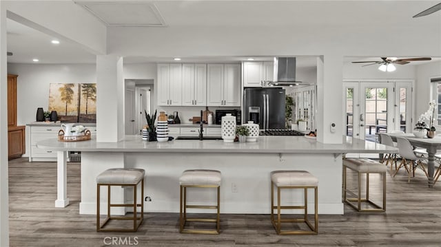 kitchen with white cabinets, stainless steel refrigerator with ice dispenser, ventilation hood, and a kitchen breakfast bar