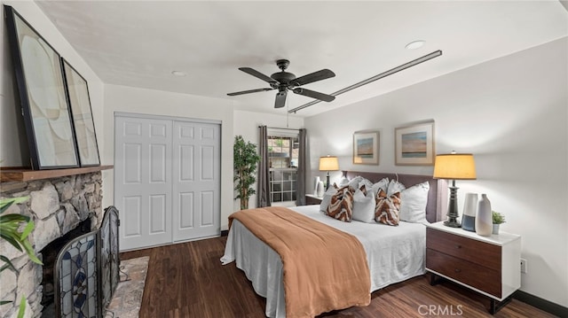 bedroom featuring a closet, a stone fireplace, ceiling fan, and dark wood-type flooring