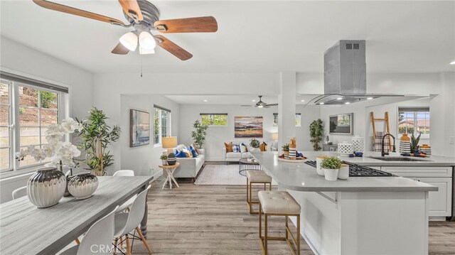 15757 Creswick Dr, La Mirada, CA 90638 - kitchen with island exhaust hood, a ceiling fan, a sink, light wood-style flooring, and white cabinets