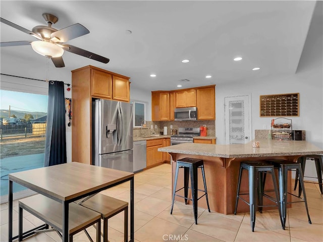 kitchen featuring decorative backsplash, a kitchen breakfast bar, stainless steel appliances, light tile patterned floors, and ceiling fan