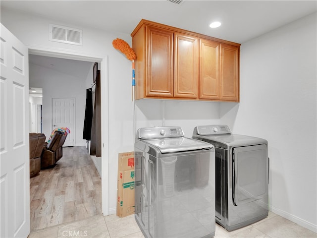 clothes washing area with washer and clothes dryer, light hardwood / wood-style flooring, and cabinets