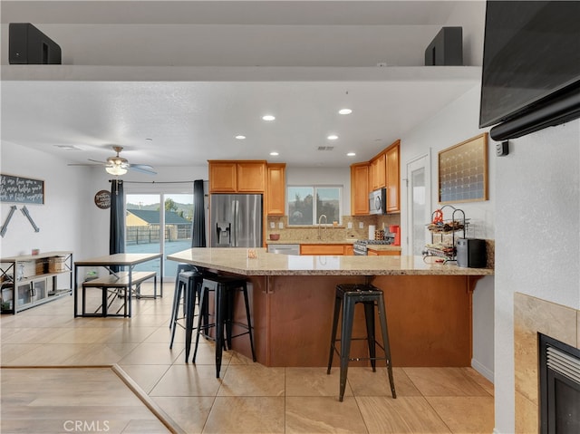 kitchen with light stone countertops, appliances with stainless steel finishes, a breakfast bar, and decorative backsplash