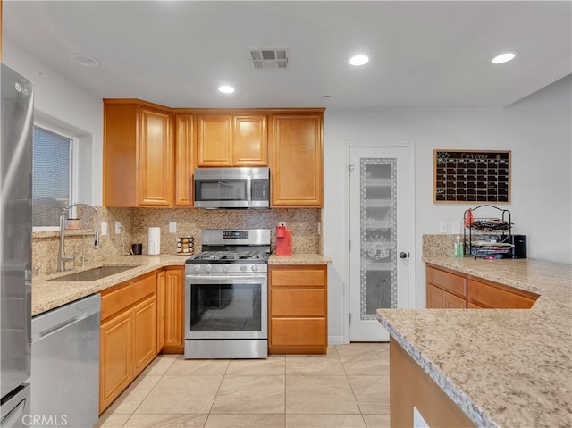 kitchen with tasteful backsplash, light tile patterned floors, appliances with stainless steel finishes, light stone countertops, and sink