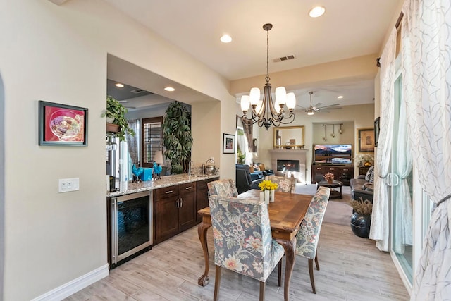 dining room with wine cooler, light hardwood / wood-style flooring, and ceiling fan with notable chandelier