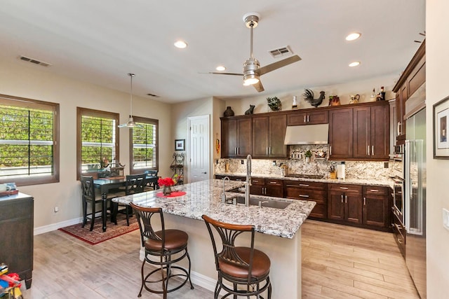 kitchen featuring light stone countertops, light wood-type flooring, sink, and an island with sink