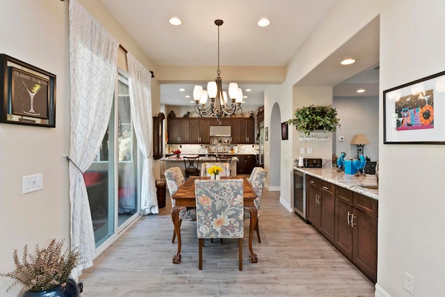 dining space with light hardwood / wood-style floors, wine cooler, and a notable chandelier