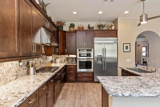 kitchen with ventilation hood, sink, light hardwood / wood-style flooring, light stone countertops, and appliances with stainless steel finishes