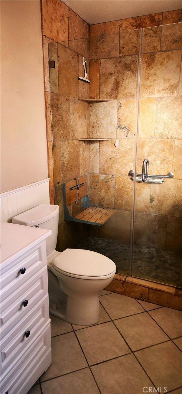 bathroom featuring tile patterned flooring, a shower with door, vanity, and toilet