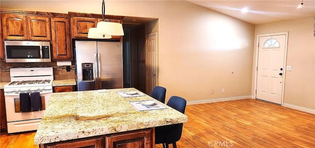 kitchen with appliances with stainless steel finishes, light stone counters, light hardwood / wood-style floors, hanging light fixtures, and a breakfast bar area