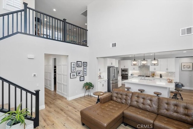 living room with sink, light hardwood / wood-style flooring, and a towering ceiling