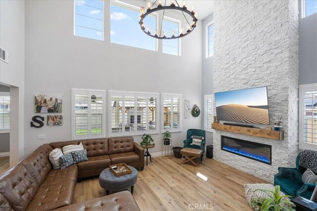 living room with a chandelier, hardwood / wood-style floors, a stone fireplace, and a towering ceiling