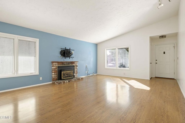 unfurnished living room with a brick fireplace, lofted ceiling, a textured ceiling, and light hardwood / wood-style flooring