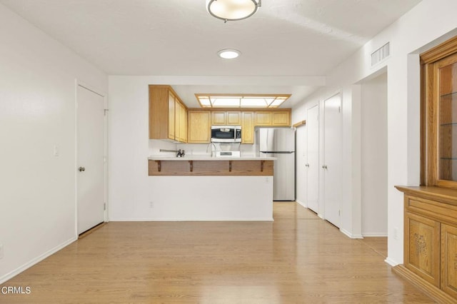 kitchen featuring kitchen peninsula, stainless steel appliances, light brown cabinetry, and light hardwood / wood-style flooring