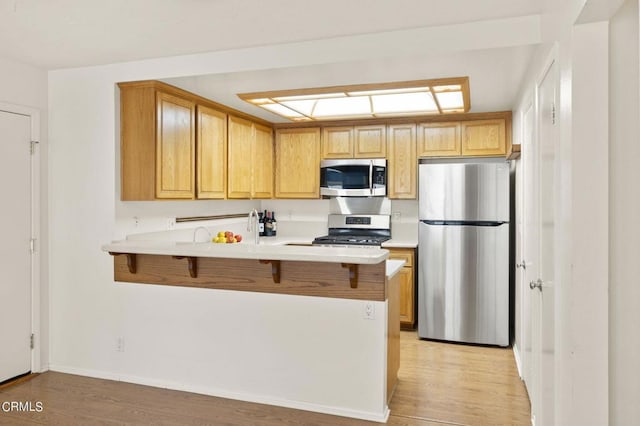 kitchen featuring kitchen peninsula, appliances with stainless steel finishes, light hardwood / wood-style floors, and a kitchen breakfast bar