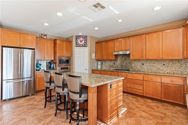 kitchen with light stone countertops, a center island, decorative backsplash, a breakfast bar, and appliances with stainless steel finishes