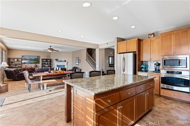 kitchen featuring light stone countertops, ceiling fan, a center island, stainless steel appliances, and decorative backsplash