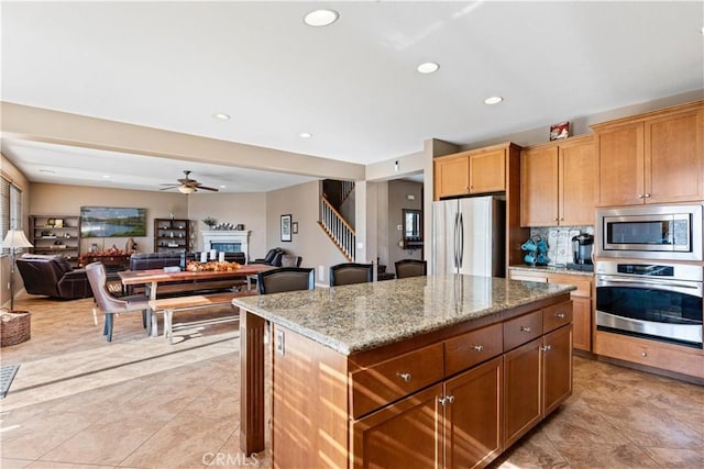 kitchen with light stone countertops, ceiling fan, stainless steel appliances, backsplash, and a kitchen island