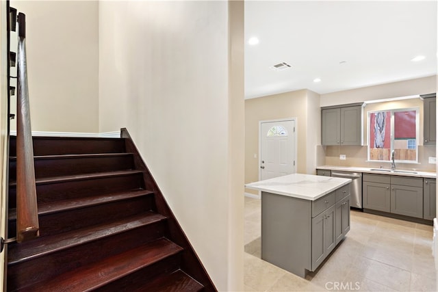 kitchen with a kitchen island, light stone countertops, dishwasher, gray cabinets, and sink