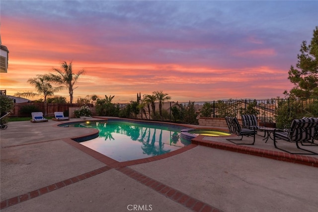 pool at dusk with an in ground hot tub and a patio