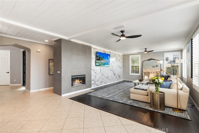 tiled living room featuring ceiling fan, wooden ceiling, ornamental molding, and a tiled fireplace