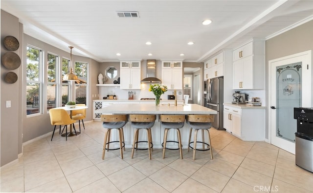 kitchen featuring backsplash, an island with sink, stainless steel fridge, white cabinets, and wall chimney exhaust hood