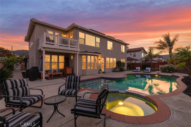 back house at dusk with a balcony, a pool with hot tub, and a patio