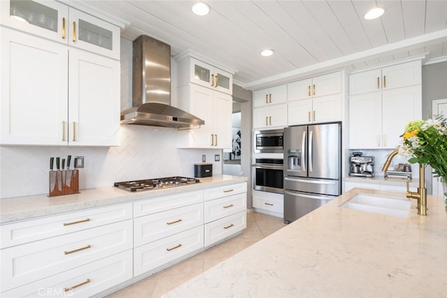 kitchen with white cabinets, wall chimney exhaust hood, stainless steel appliances, backsplash, and light stone counters