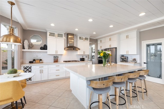 kitchen with white cabinetry, stainless steel fridge, backsplash, a kitchen island with sink, and wall chimney exhaust hood