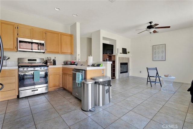 kitchen featuring kitchen peninsula, light tile patterned floors, appliances with stainless steel finishes, a fireplace, and ceiling fan