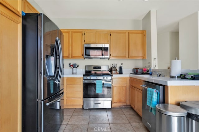 kitchen featuring tile countertops, tile patterned floors, appliances with stainless steel finishes, and light brown cabinets