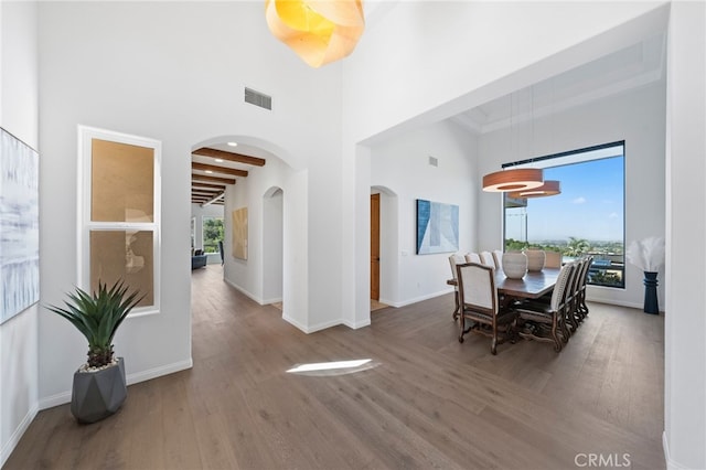 dining room featuring a towering ceiling, beam ceiling, and hardwood / wood-style flooring