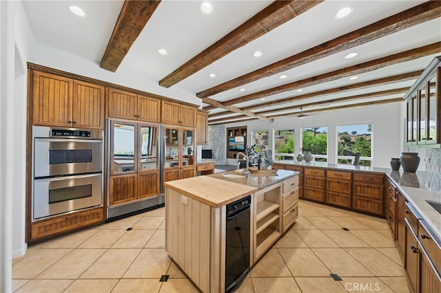 kitchen featuring beam ceiling, double oven, butcher block counters, and a center island with sink