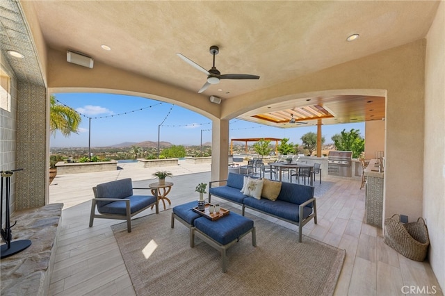 view of patio / terrace with exterior kitchen, grilling area, ceiling fan, an outdoor living space, and a mountain view