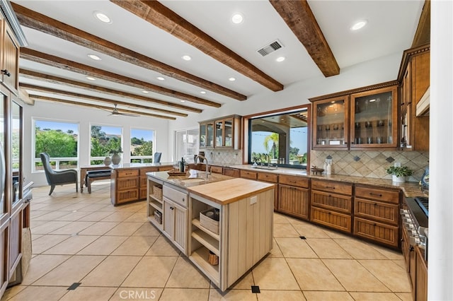 kitchen featuring beamed ceiling, an island with sink, backsplash, sink, and butcher block countertops