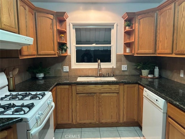 kitchen with backsplash, sink, white appliances, light tile patterned floors, and dark stone counters