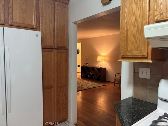 kitchen with white refrigerator, dark stone counters, light hardwood / wood-style floors, backsplash, and stove