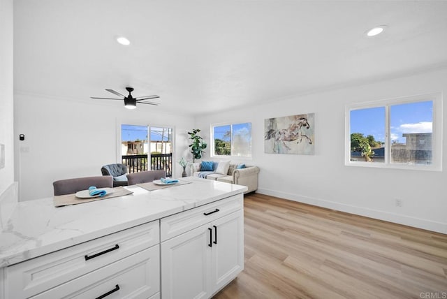 kitchen with light stone countertops, light hardwood / wood-style flooring, white cabinets, and ceiling fan