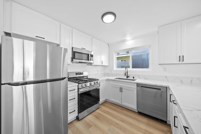 kitchen with light stone countertops, white cabinetry, sink, stainless steel appliances, and light hardwood / wood-style flooring