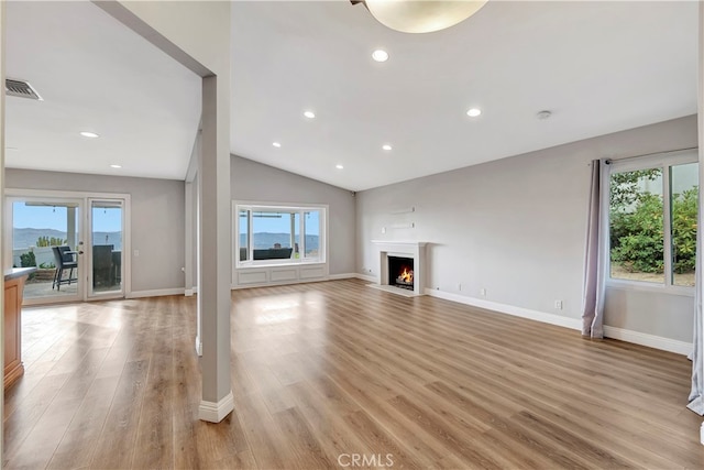 unfurnished living room with vaulted ceiling, a healthy amount of sunlight, and light hardwood / wood-style floors