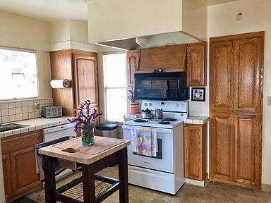 kitchen featuring dishwashing machine, tile counters, white electric range, wall chimney exhaust hood, and decorative backsplash