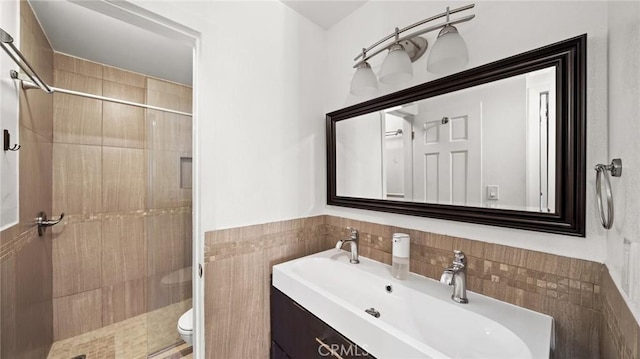 bathroom with vanity, toilet, a shower with shower door, and tile walls