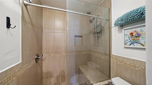 bathroom featuring tiled shower, toilet, and tile walls