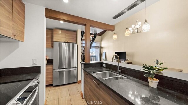 kitchen featuring stainless steel refrigerator, sink, dark stone countertops, stove, and pendant lighting