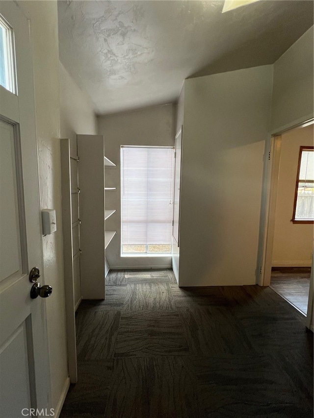 corridor featuring a textured ceiling, vaulted ceiling, and dark colored carpet