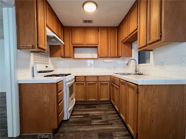 kitchen featuring sink, backsplash, gas range gas stove, tile counters, and dark wood-type flooring