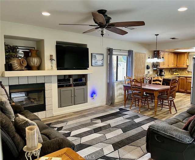 living room with light hardwood / wood-style flooring, a tile fireplace, and ceiling fan